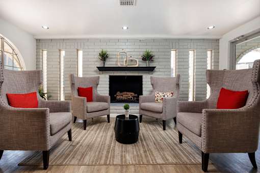Four chairs with red pillows are arranged around a fireplace.