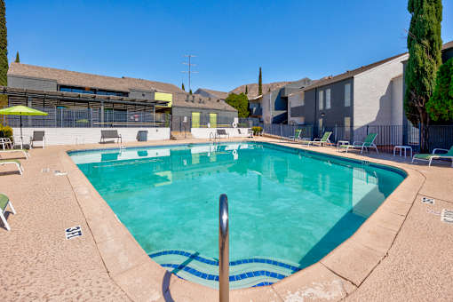 A swimming pool surrounded by chairs and trees.