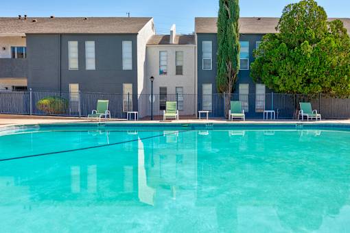 A swimming pool in front of a building with trees and chairs around it.
