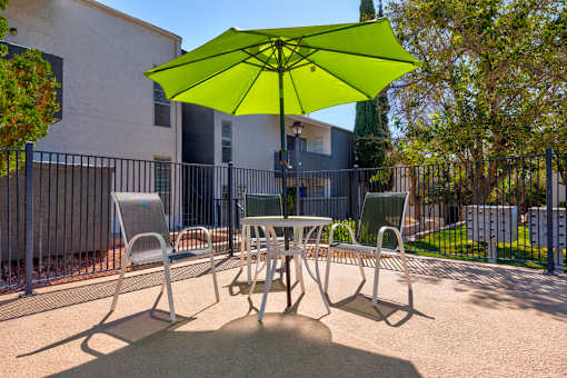 A green umbrella shades a table and chairs in a courtyard.