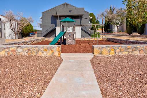 A playground area with a slide and a building in the background.