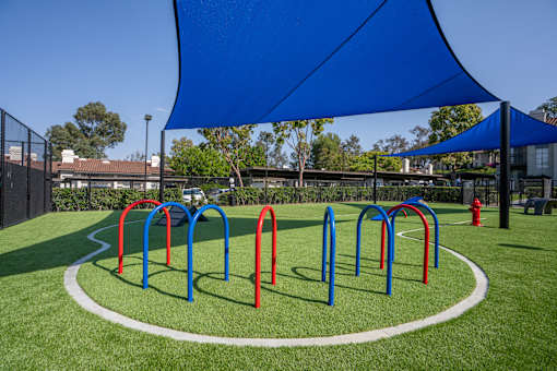 A playground with a blue shade structure and red and blue swings.