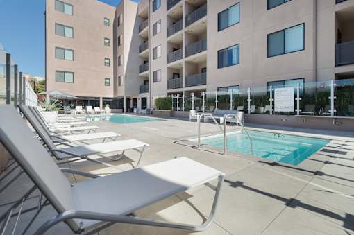 A pool area with sun loungers and a building in the background at Wilshire Valencia Apartment, Los Angeles, CA