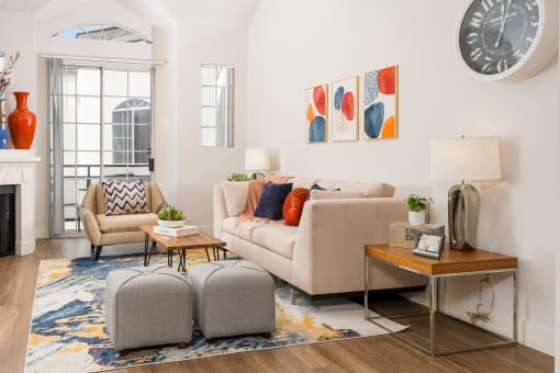 Apartments for Rent in Miracle Mile Los Angeles, CA - The Preston - Living Room with Plank Wood Style Flooring, Area Rug, Sofa, Ottoman Stools, Armchair, Side Table with Lamps, Coffee Table, High Ceiling, and Glass Door with Access to Balcony.