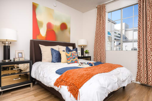 Two-Bedroom Apartments in Los Angeles, CA - The Preston - Bedroom with Plank Wood Style Flooring, Large Bed, Nightstands with Lamps, and Spacious Window.
