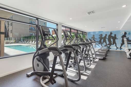 A row of treadmills in a gym with a mural of running people on the wall at Wilshire Valencia Apartment, Los Angeles, California