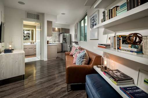A living room with a brown leather couch and a bookshelf filled with books.at Chelsea Santa Monica, Santa Monica, CA  