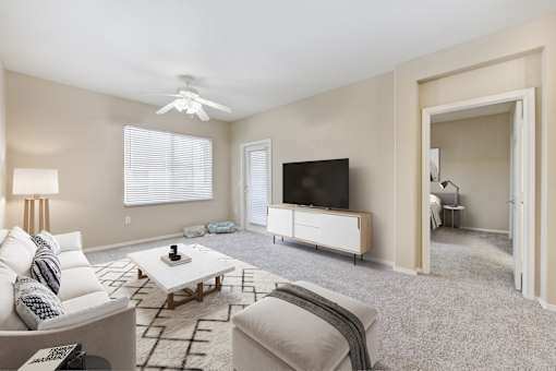2-Bedroom Apartments in Upland, CA - Park Central Apartments - Living Area with Carpet Flooring, Couch, Ottoman, Coffee Table, Side Table, Floor Lamp, Ceiling Fan, Media Console, and Television.