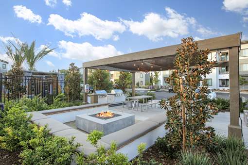 A patio with a fire pit surrounded by plants.