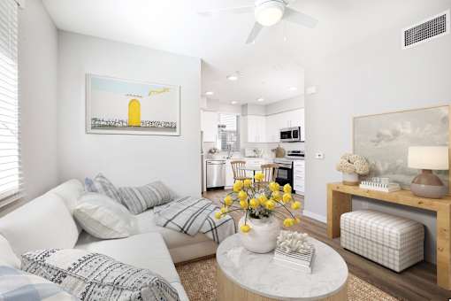 Pet-Friendly Apartments in West Sacramento, CA - The Strand - Living Room with Ceiling Fan, Wood-Style Flooring, Area Rug, Sectional Couch, Circular Coffee Table, Armchair, White Walls, and Large Window.
