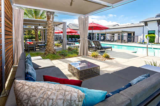 A patio with a couch, pillows, and a pool in the background.