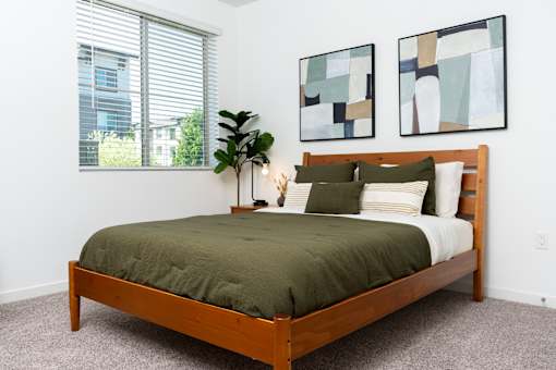 A bedroom with a bed, pillows, a plant, and two paintings on the wall.