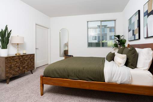 A bedroom with a bed, nightstand, and a plant.