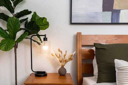 A modern bedroom with a wooden headboard and a side table with a lamp and a plant.