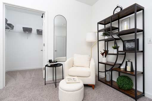 A white chair sits in front of a mirror in a room with a shelf.