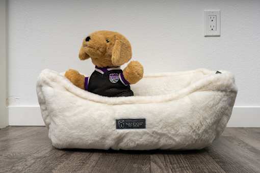 A dog bed with a stuffed dog wearing a purple shirt.