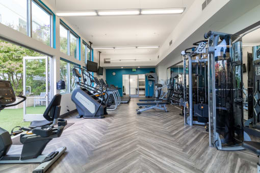 a gym with cardio machines and weights in a building with large windows