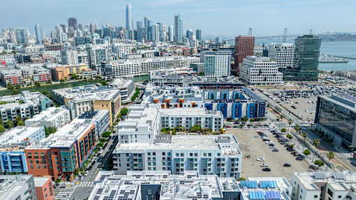 A cityscape with a mix of modern and older buildings, a parking lot, and a body of water in the distance.