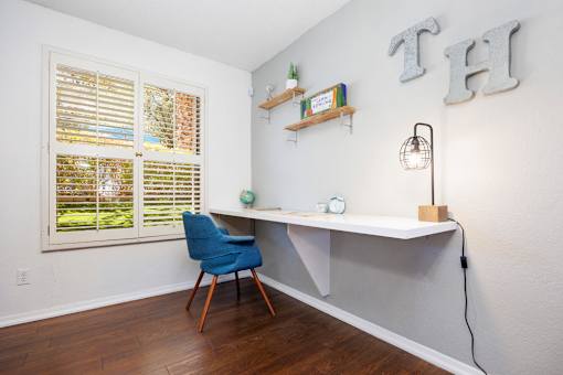 A room with a desk, chair, and shelves with plants.
