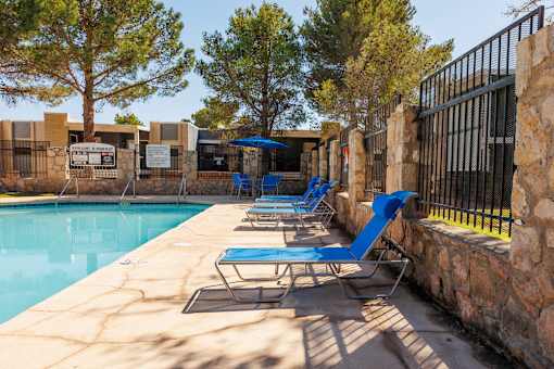 A pool with blue chairs and a stone wall.