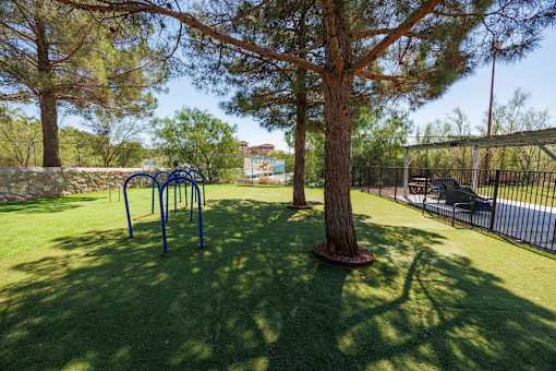A playground with a swing set and a tree in the middle of a grassy area.