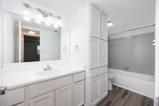 A white bathroom with a sink, mirror, and bathtub.