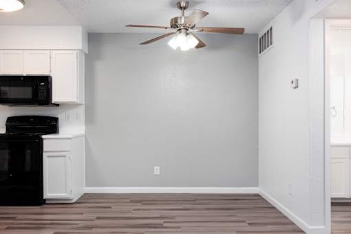 A kitchen with a black microwave and oven, white cabinets, and a ceiling fan.