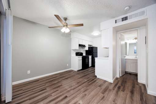 A room with a ceiling fan and a kitchen area in the background.