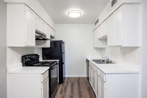 A black refrigerator is in a kitchen with white cabinets.