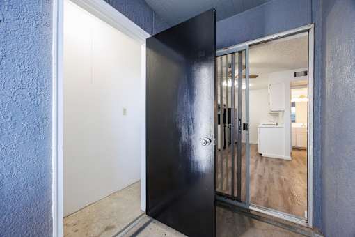 A black door with a glass window is open to a room with a white fridge.