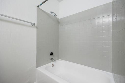 A white bathtub in a bathroom with grey tiled walls.