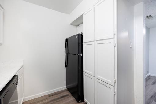 A black refrigerator is in a kitchen with white cabinets.