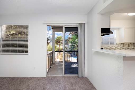 A room with a carpeted floor, a window with blinds, and a sliding glass door leading to a balcony.