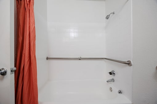A white bathroom with a shower and orange curtain.