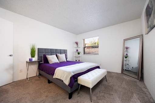 A bedroom with a purple bed and a white chair.
