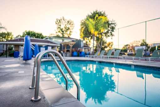 A pool with a ladder in the foreground and people in the background at Nola 624 Apartments, California, 91790