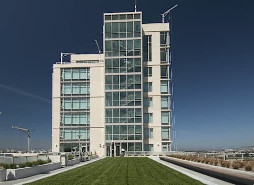 A modern building with a glass facade and a green lawn in front at The Grand Apartments, Oakland 94612