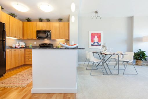 A kitchen with wooden cabinets and a white island with a dining table and chairs at The Grand Apartments, Oakland, California