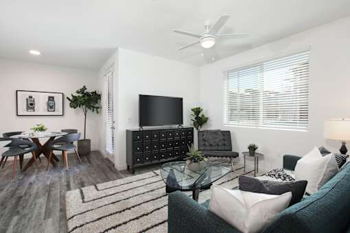 A living room with a grey couch, a glass table, a television, and a ceiling fan.