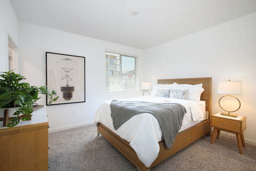 Apartments in West Sacramento, CA, with In-Unit Washer and Dryer - The Strand - Bedroom with Carpeted Flooring, Bed, Wooden Nightstands with Lamps, Dresser, White Walls, and Window.