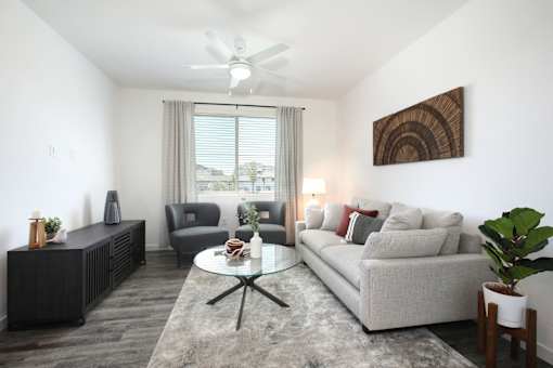 A living room with a grey couch, a coffee table, a fan, and a painting on the wall.