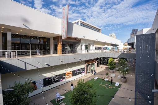 A view of a shopping mall with a green lawn and people walking around.