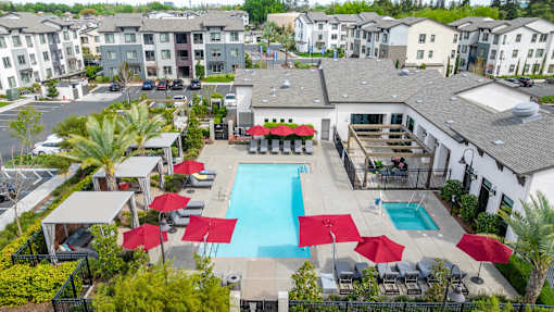 A pool surrounded by red umbrellas and lounge chairs.