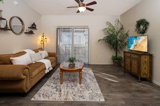 1 Bedroom Apartments in Surprise, AZ - The Village at West Point - Living Room With A Sofa And Coffee Table, Television On A Wood Console, And A Kitchen And Dining Area In The Background.