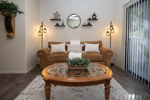 A living room with a brown couch, a round table, and a mirror on the wall.