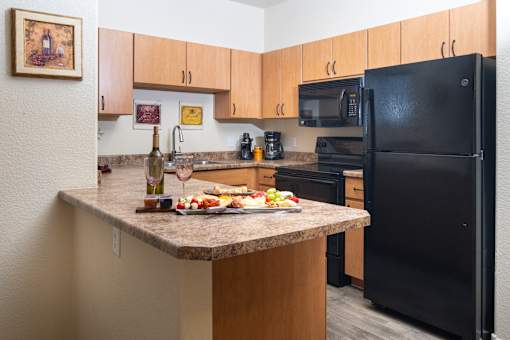 A kitchen with a black refrigerator and wooden cabinets.