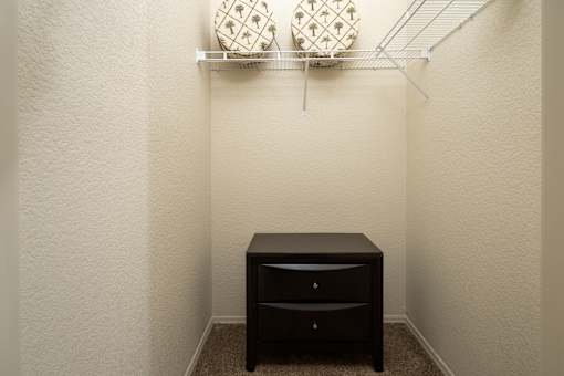 A small black desk with two drawers is in a corner of a room with white walls.