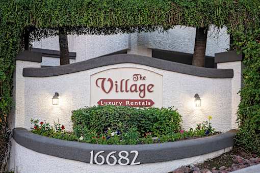 A sign for The Village Luxury Retreats is surrounded by plants and flowers.