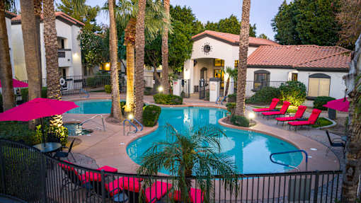 Apartments for Rent Surprise, AZ - The Village at West Point - A Swimming Pool With Palm Trees, Pink Lounge Chairs, And Umbrellas.