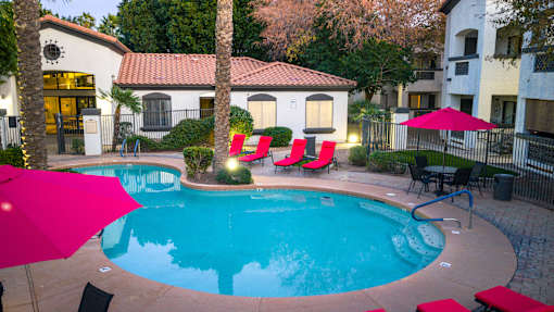 A pool surrounded by red lounge chairs and umbrellas.